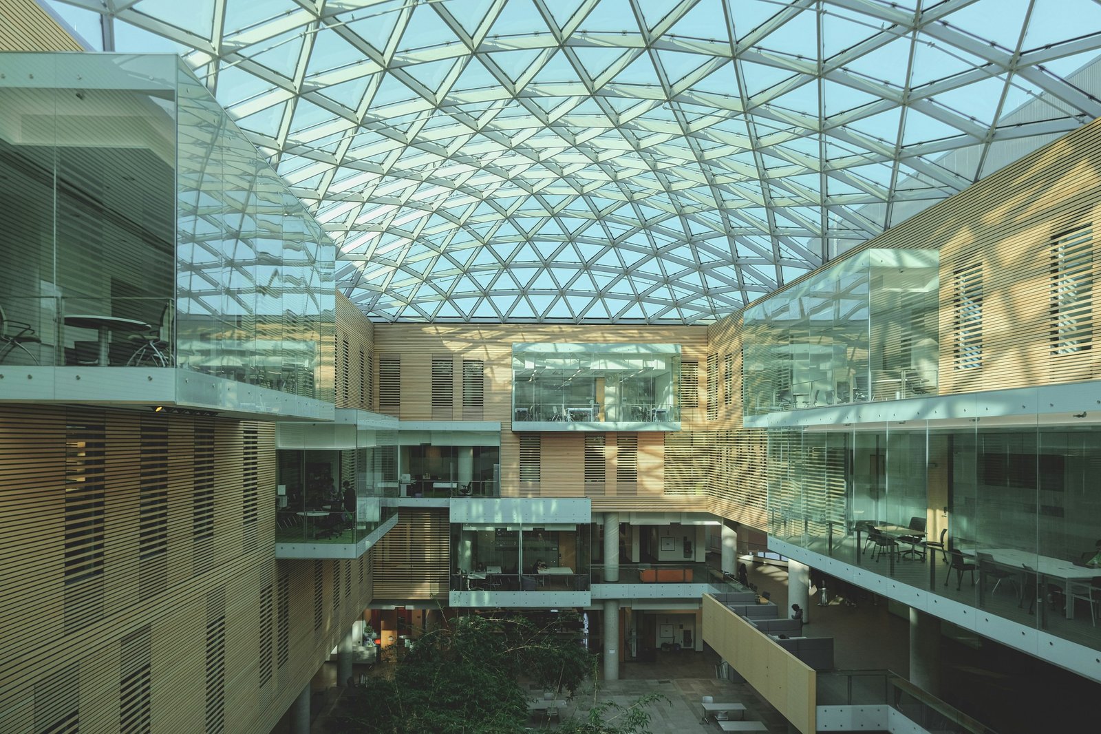 A daylight-filled university atrium with a geometric glass roof, study balconies and warm wood walls